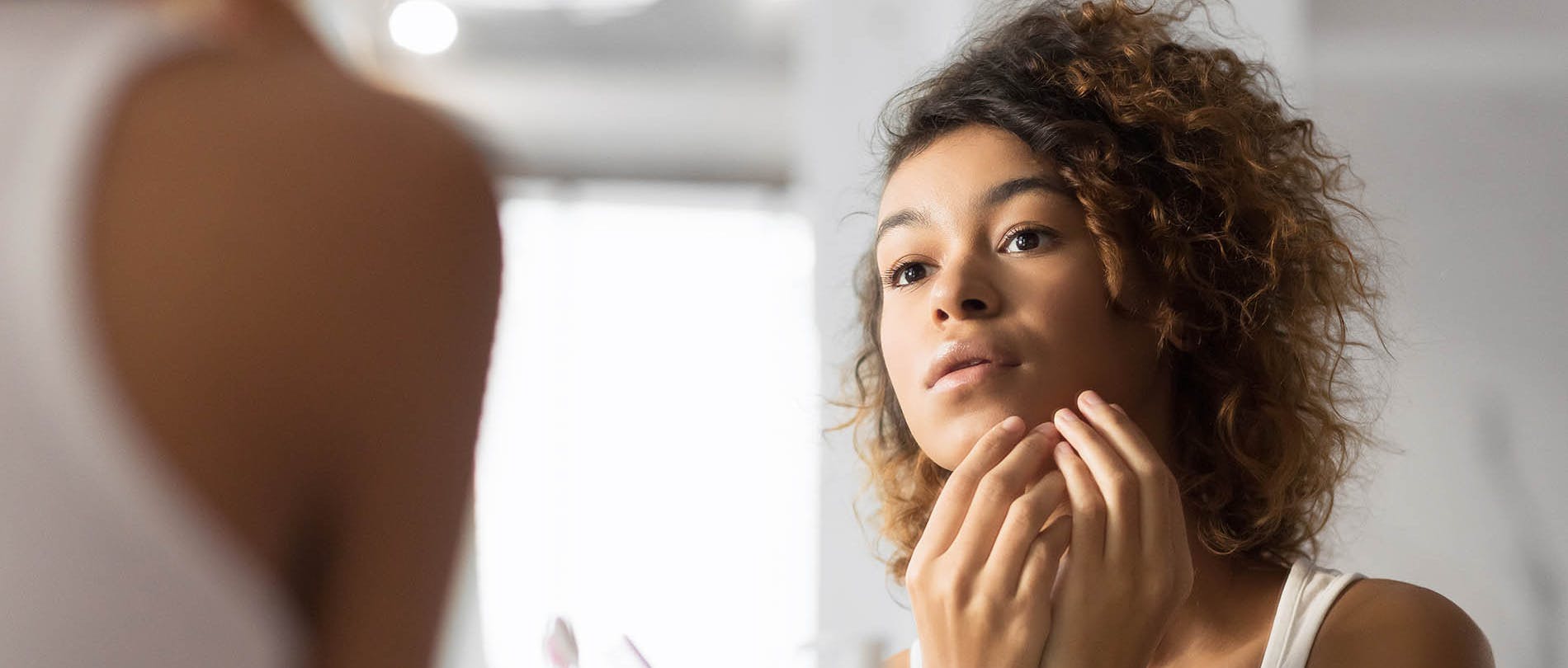 Woman Examines Acne in Mirror